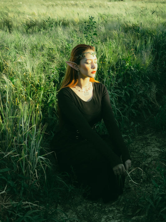 Red-haired elf woman kneels in a sunlit green field