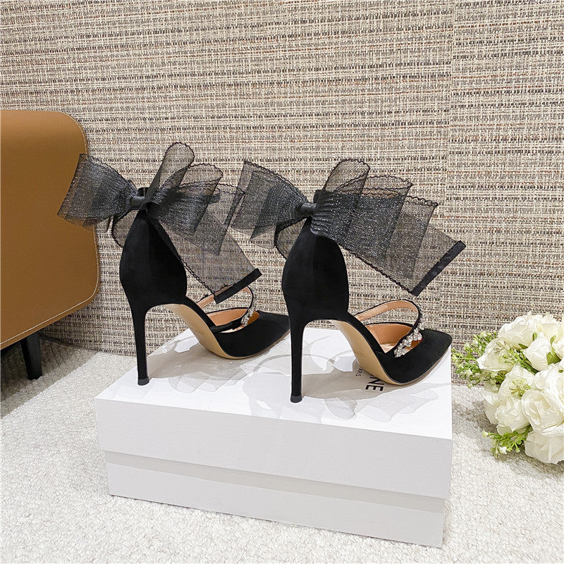 Black satin high heel sandals with bowknot design, closed with delicate straps, displayed on a white box, perfect for weddings and special occasions.