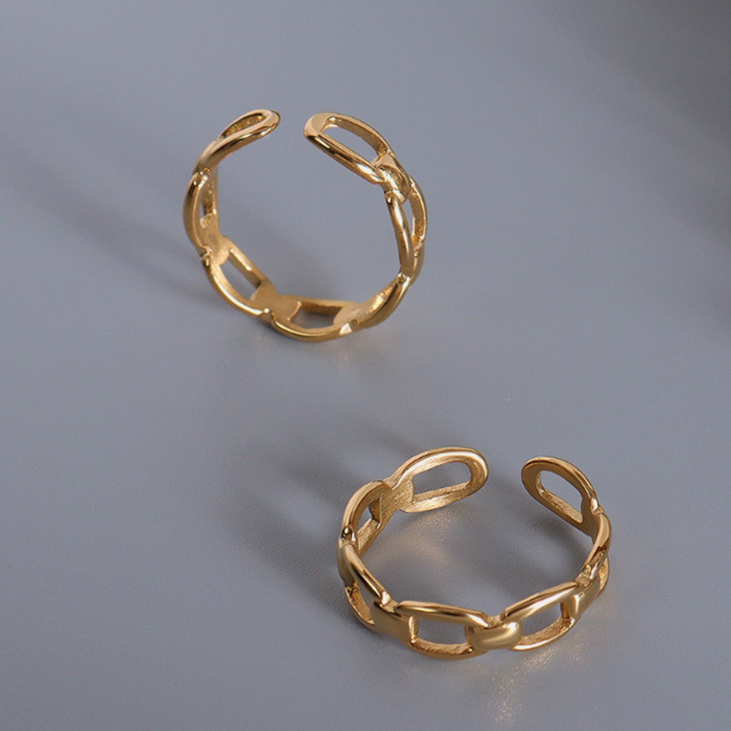 Gold-plated titanium steel adjustable ring set on a gray surface, showcasing elegant link design.